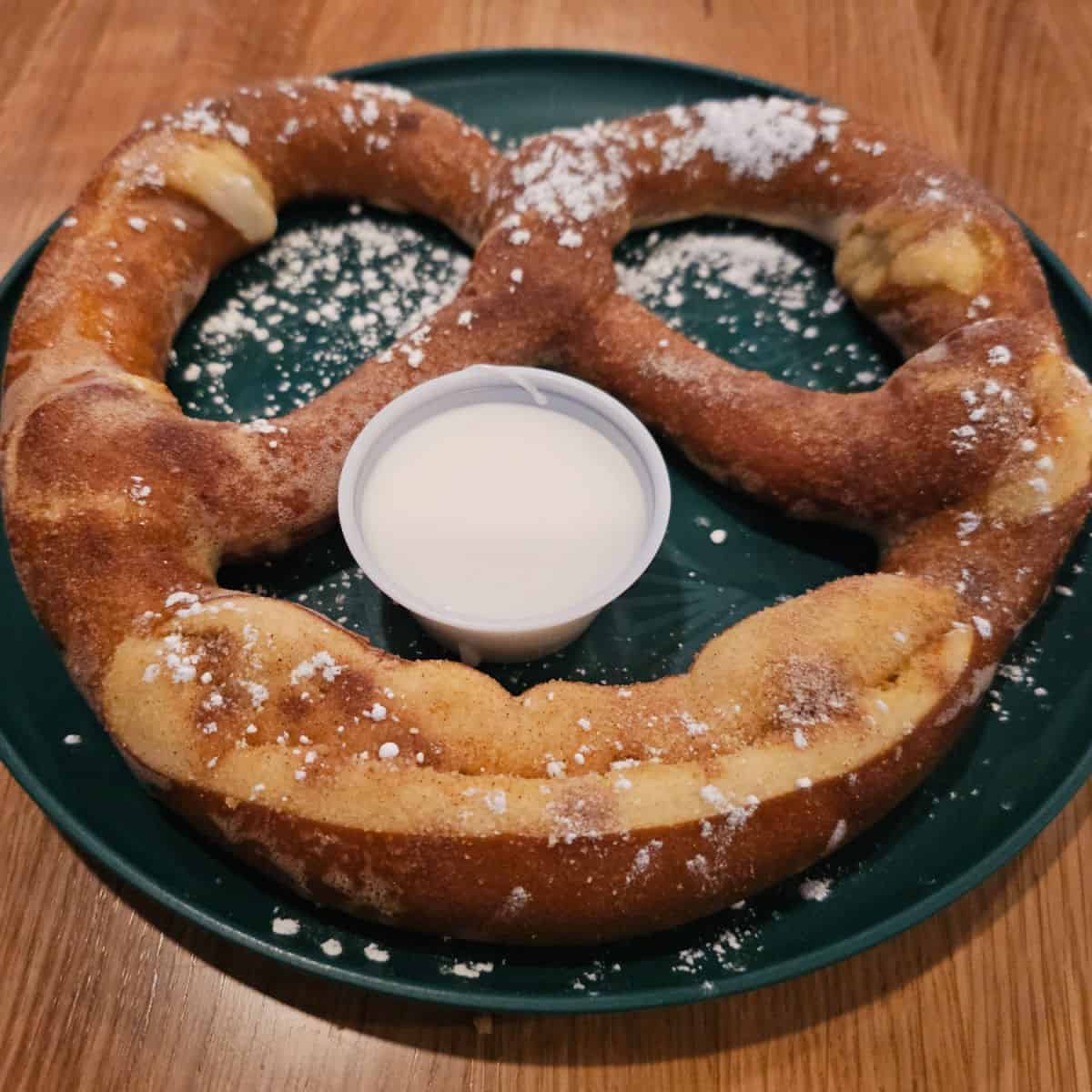 Cinnamon sugar pretzel on a dark plate with a container of icing