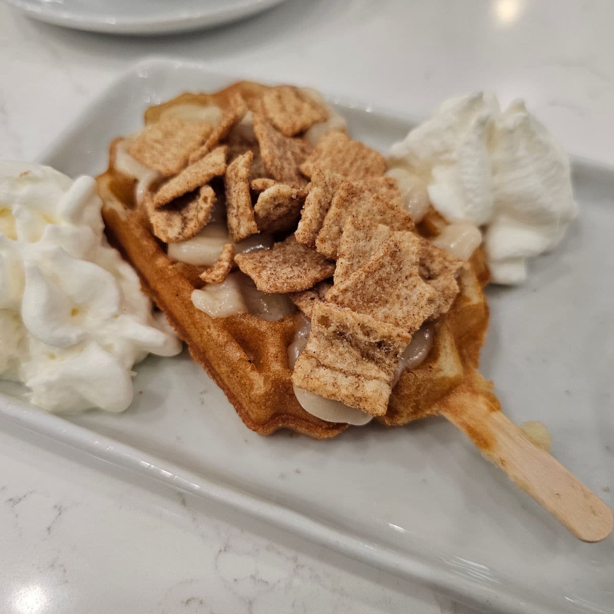 waffle pop with cinnamon toast crunch on top of it and whipped cream next to it