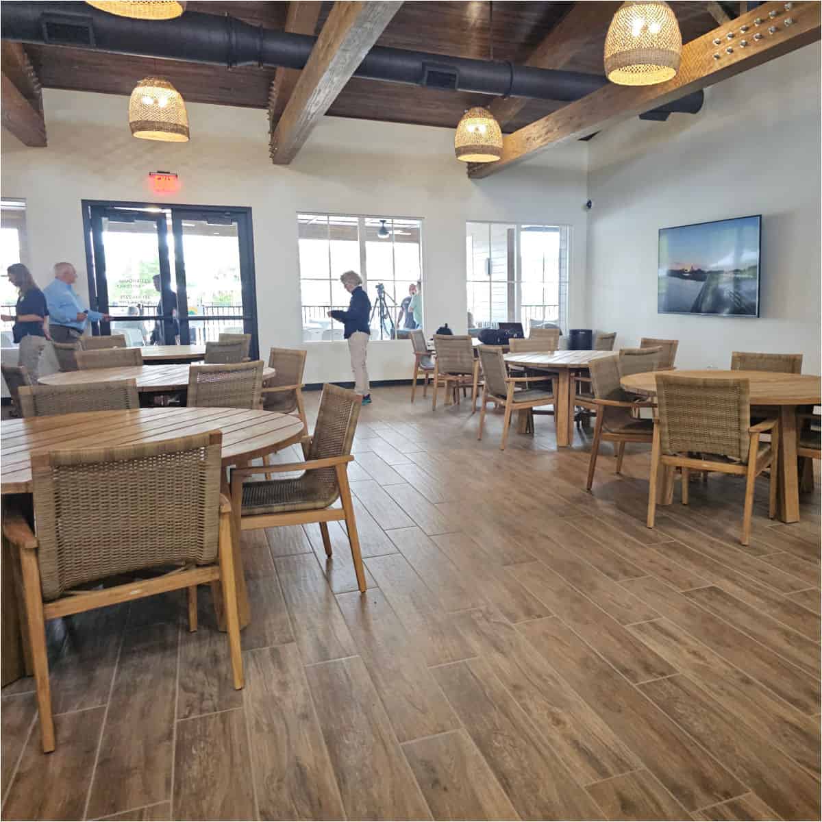 indoor seating with tables and chairs, TV on the wall , people milling around