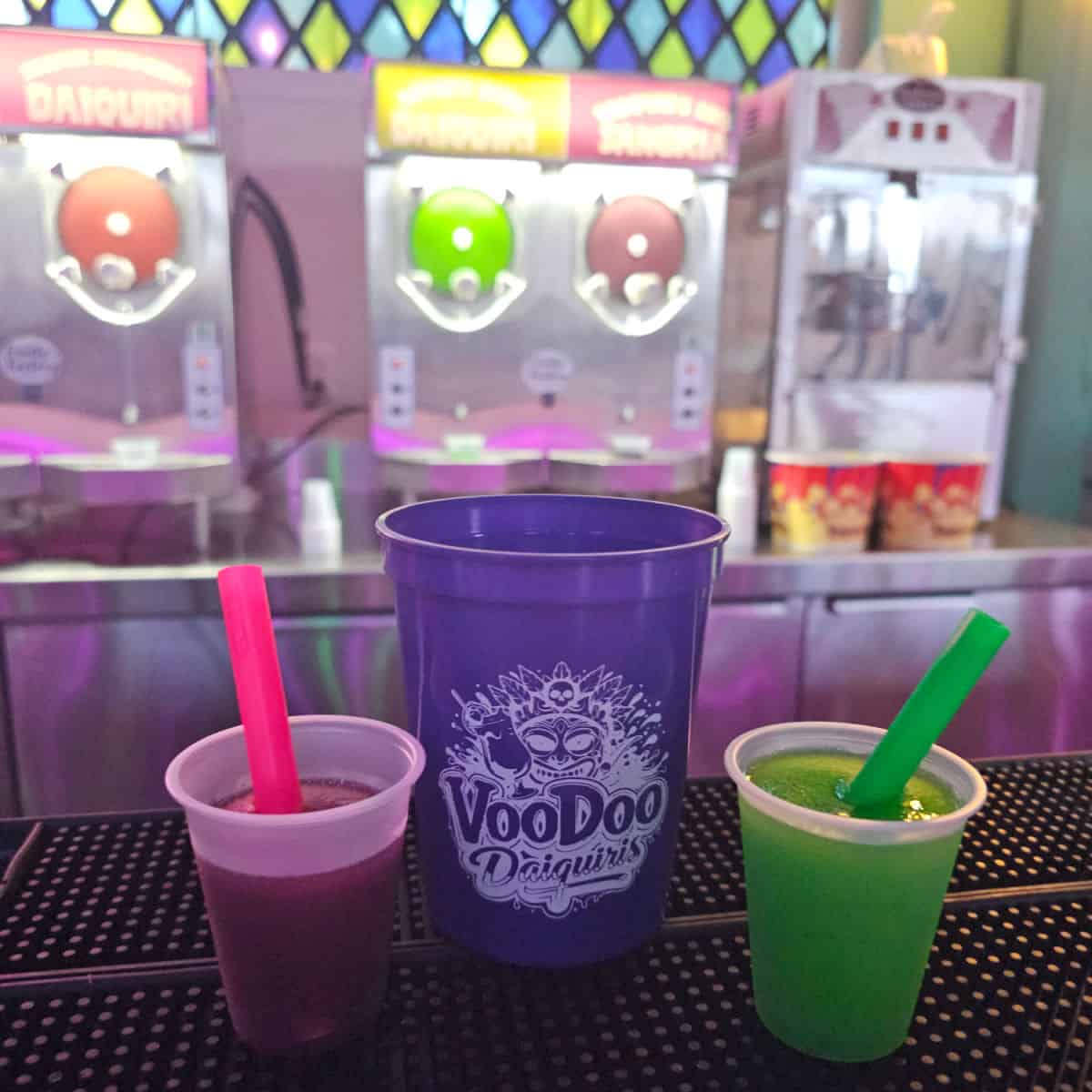 VooDoo Daiquiris purple cup next to two mini cups with drink machine in the background