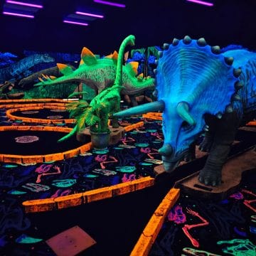 Neon dinosaur statues in the middle of mini golf course indoors