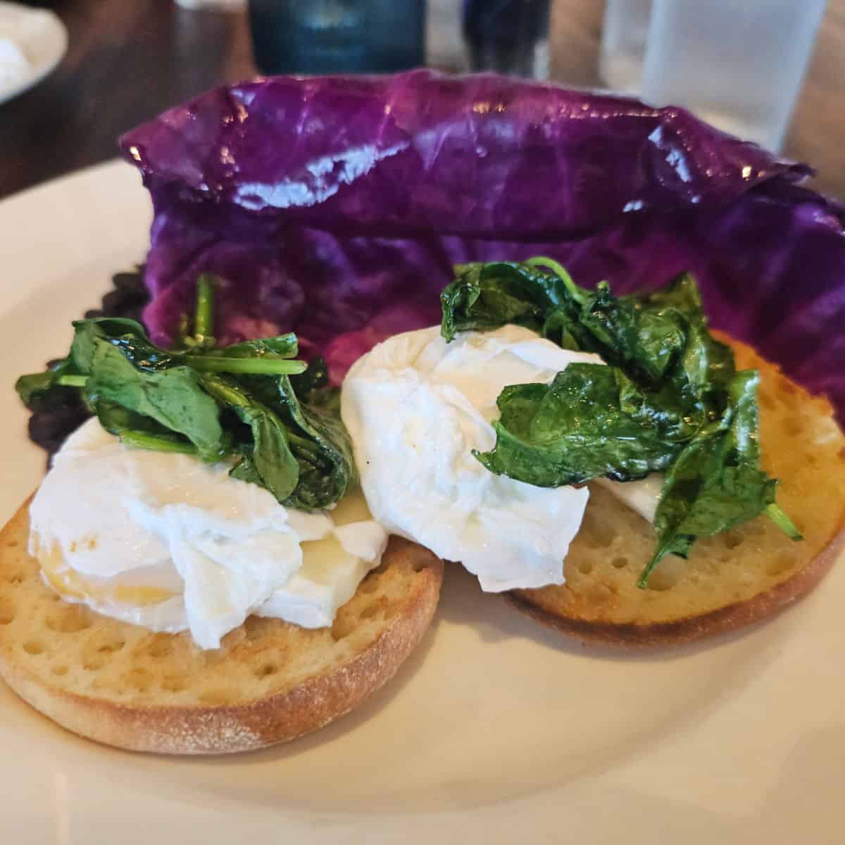 eggs and greens on english muffin with purple lettuce behind it