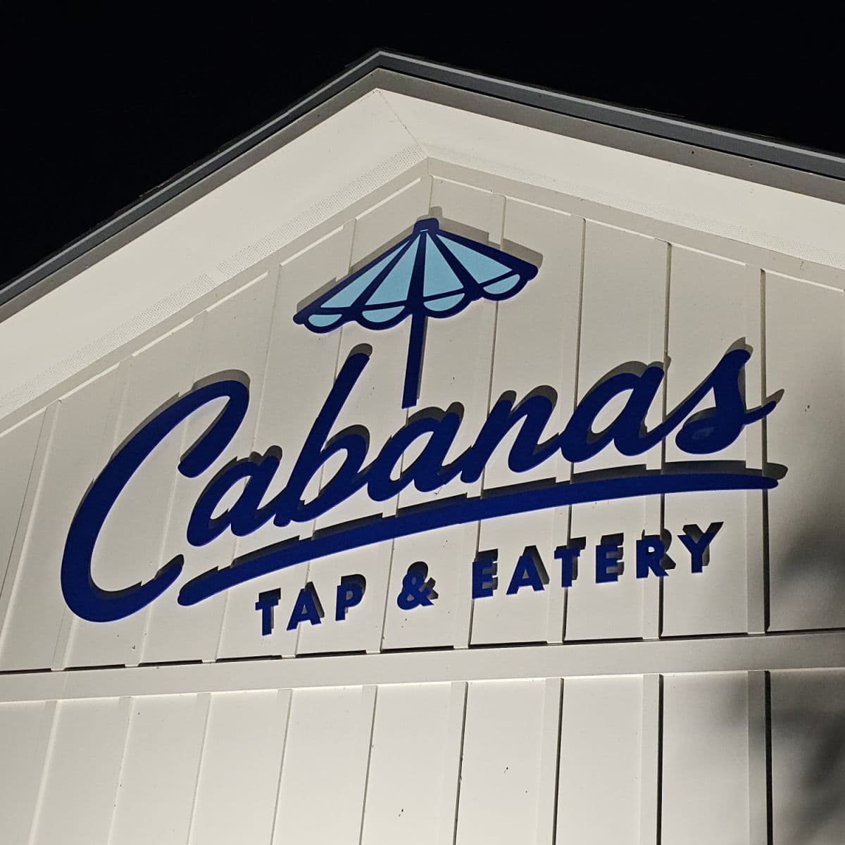 Cabanas Tap & Eatery sign on the side of a white building with a blue umbrella above the word Cabanas