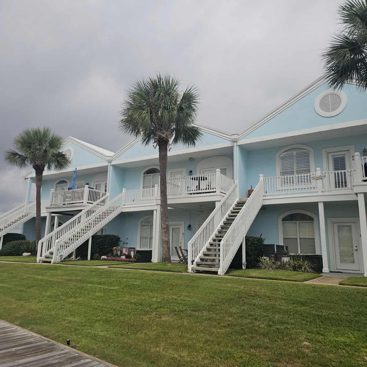 blue and white building with white stairs up to the 2nd level, palm trees between the buildings