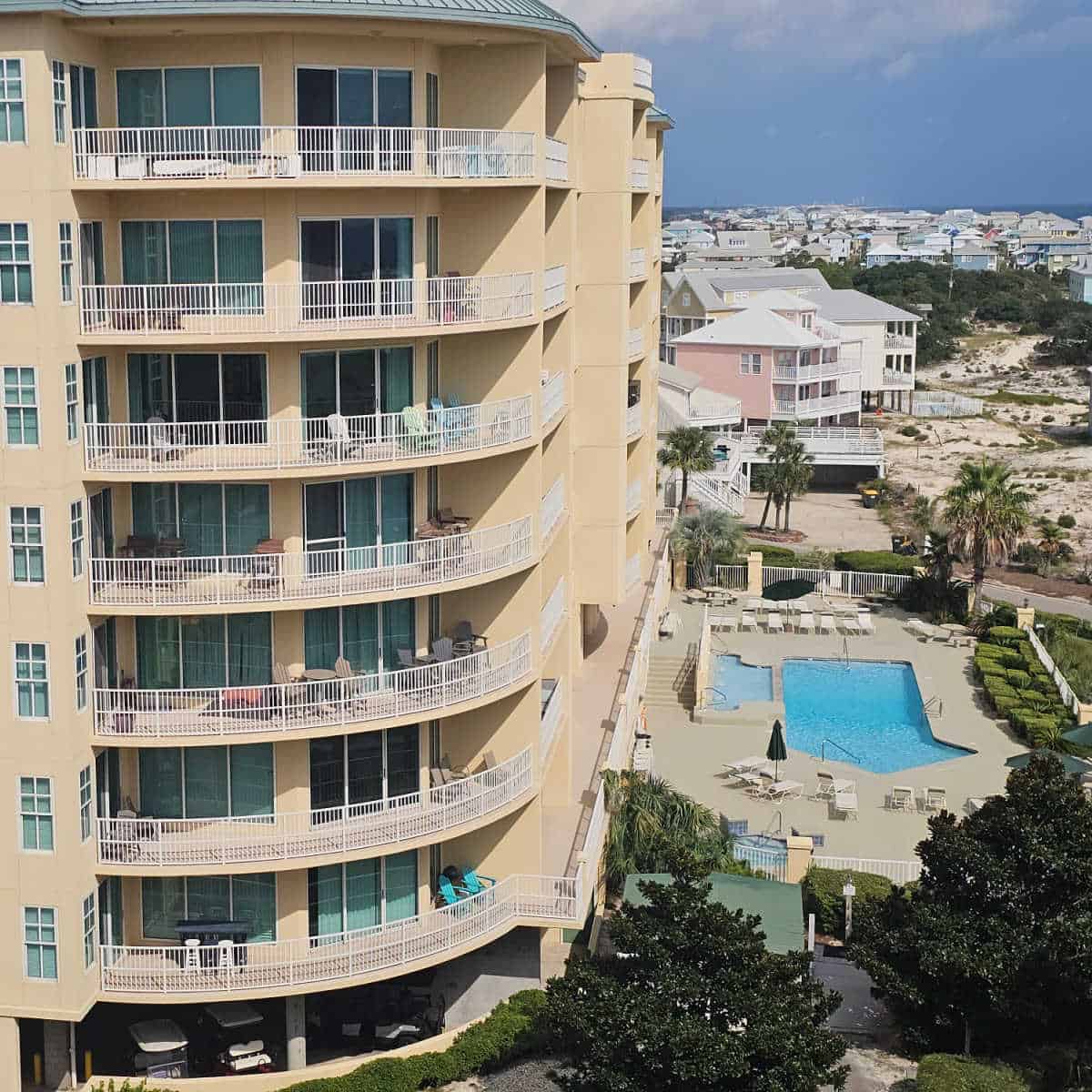 multi-story yellow condo building next to an outdoor pool and pool deck, Fort morgan houses and the Gulf in the background