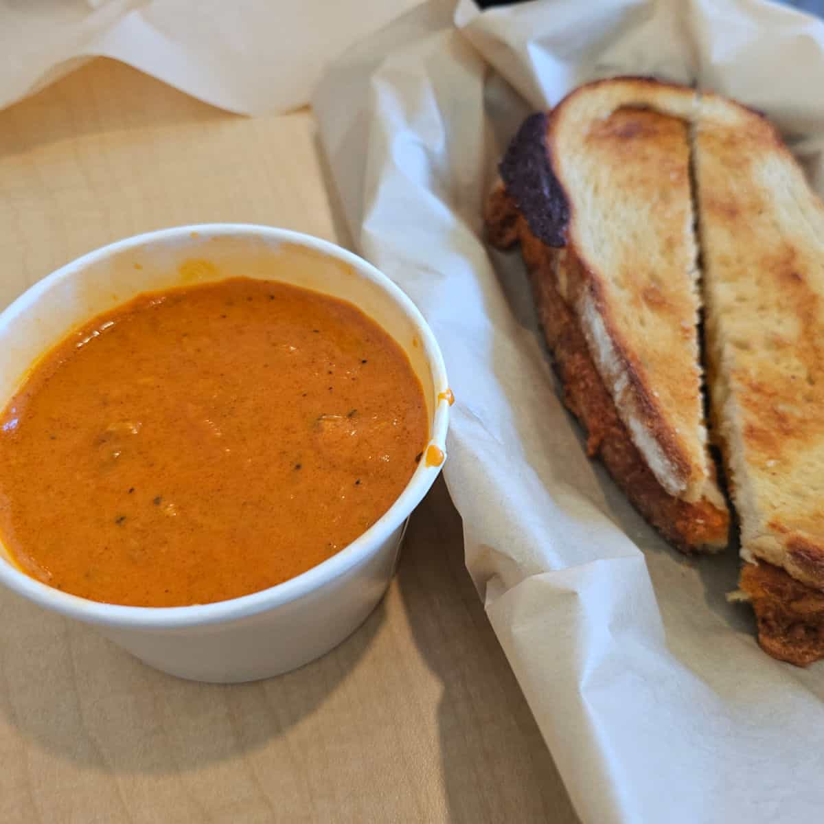 Grilled cheese on paper in a basket next to a cup of soup