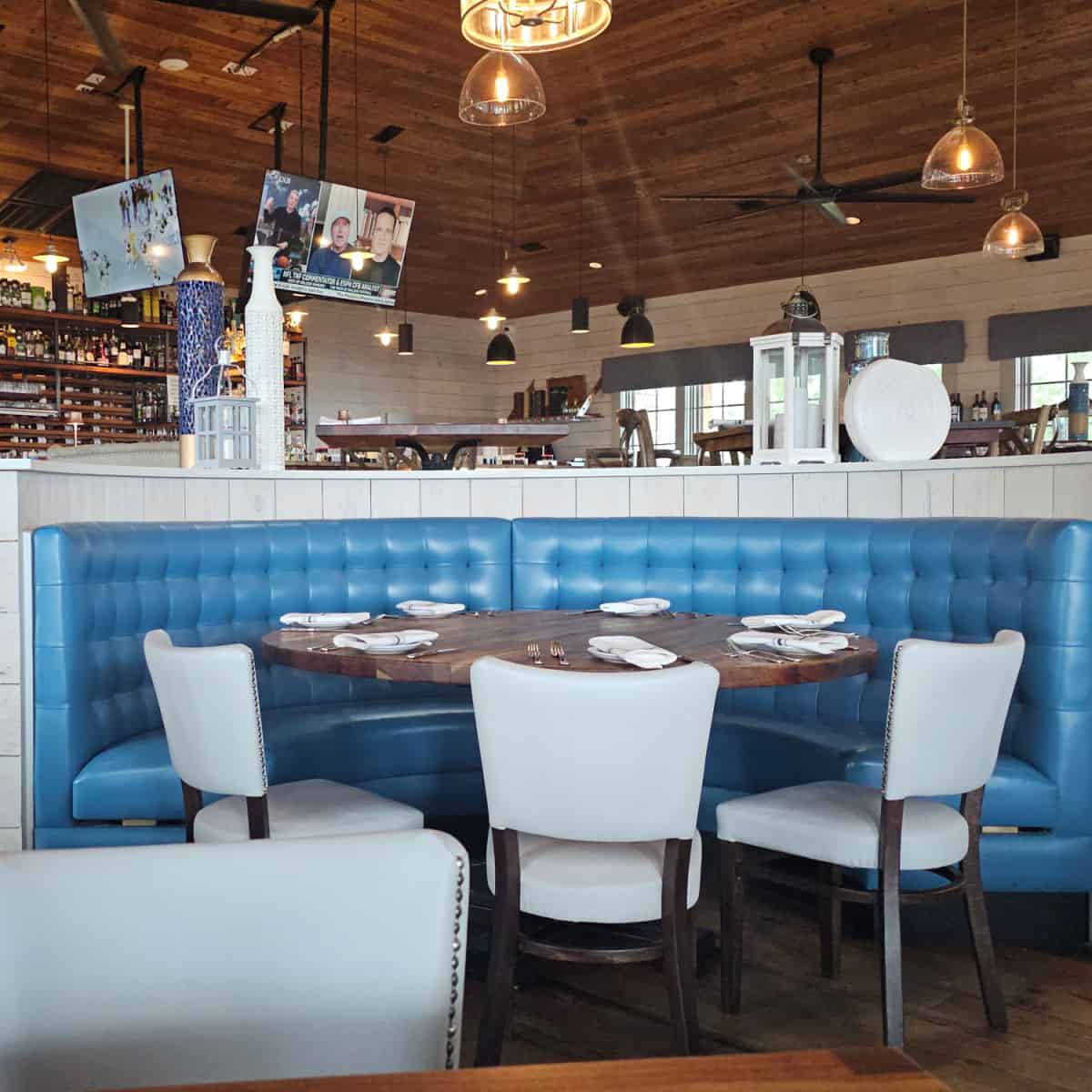 booth seating with blue leather wrap around seating and chairs pulled up to the table, Jesse's bar in the background