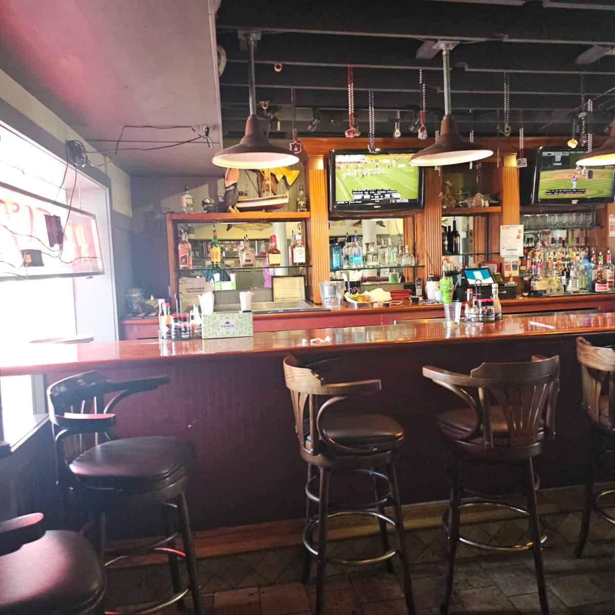 indoor bar area with shelfs filled with bottles behind the bar and tv's above the glasses and barware