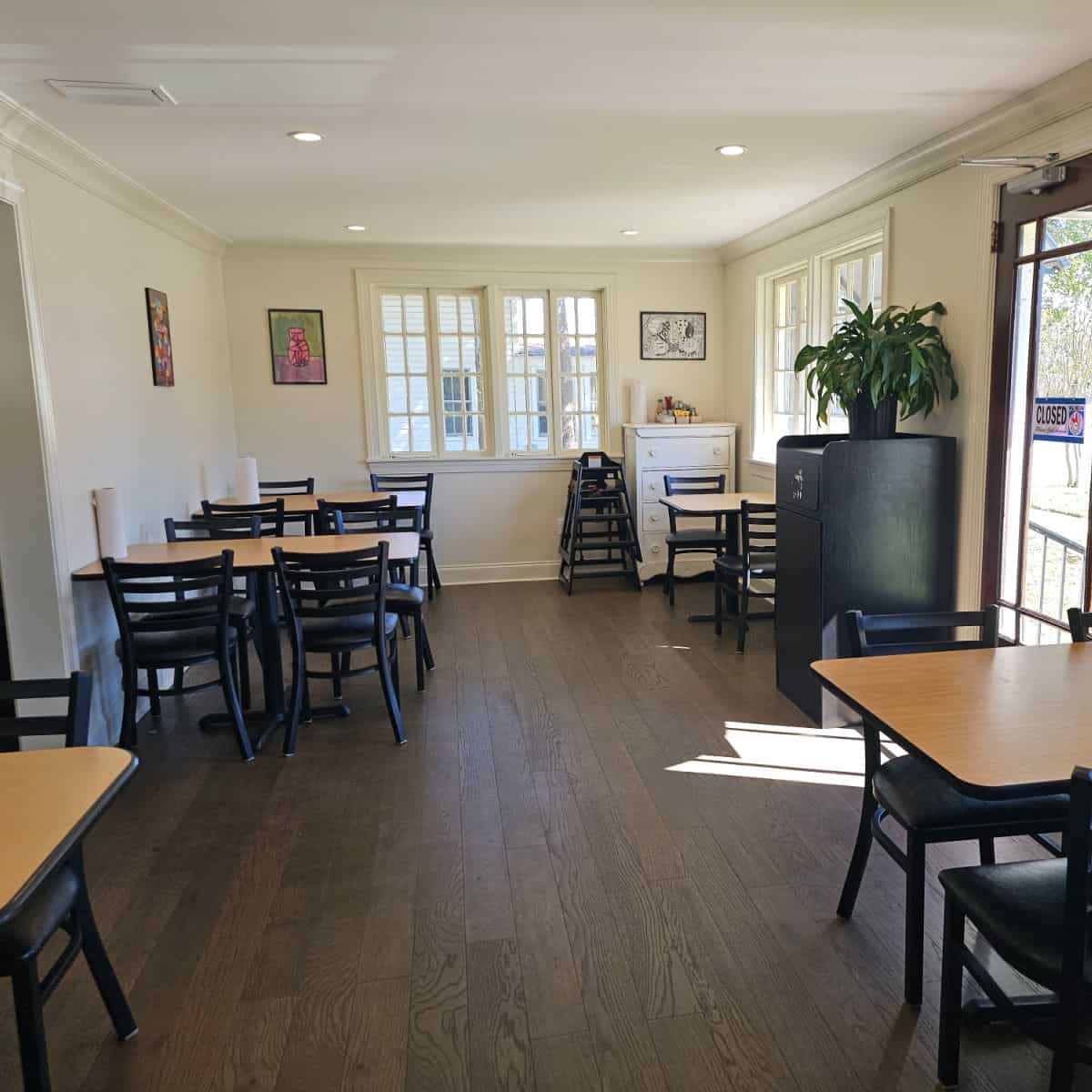 indoor seating with tables and chairs with art on the wall, plant on top of the garbage can