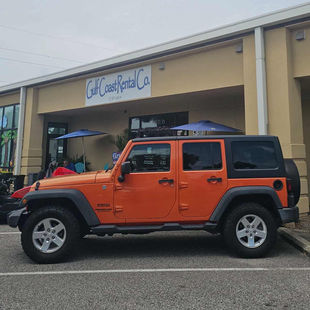 Orange 4 door Jeep parking in front of Gulf Coast Rental Co. sign and building