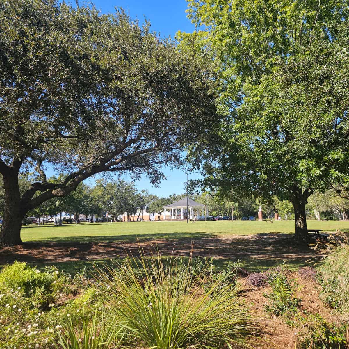 looking through trees to a grassy area and bandstand in the distance