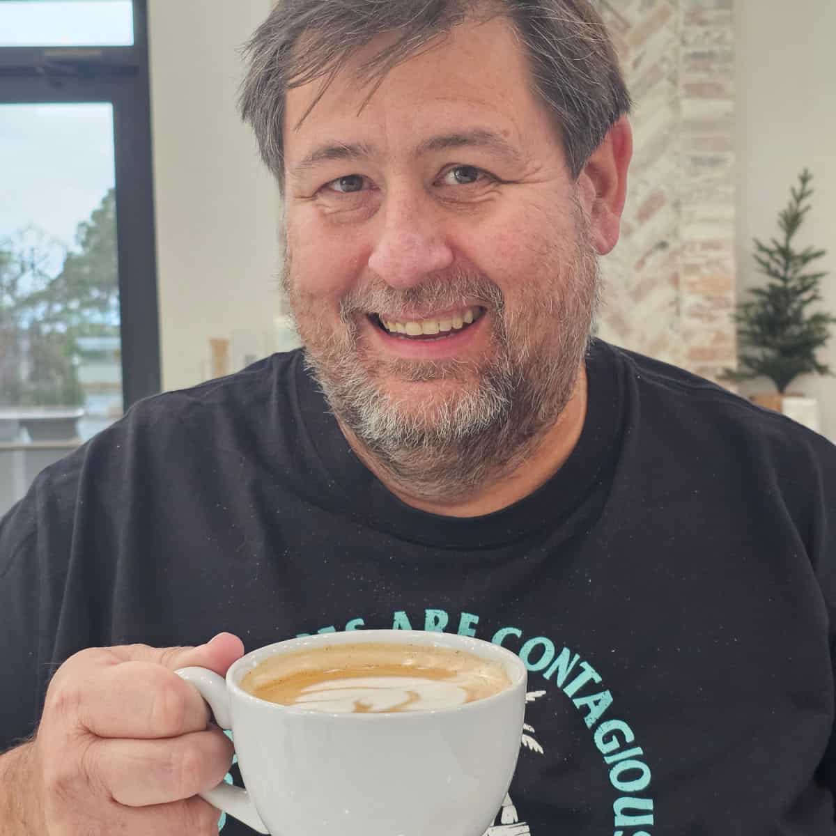 john holding a white coffee mug with a wall behind him