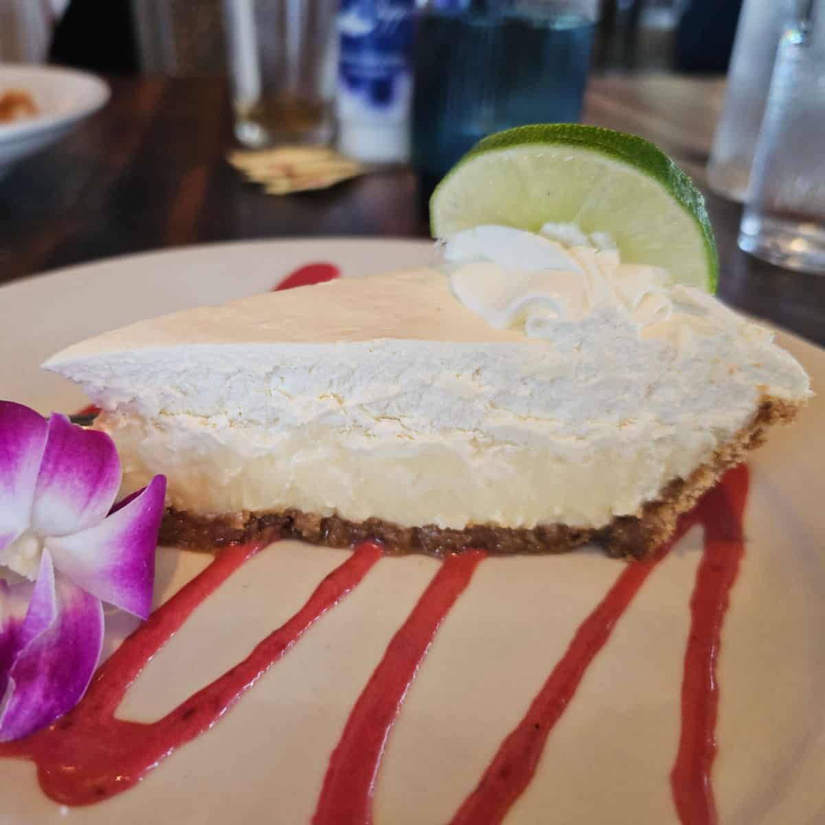key lime pie with a raspberry drizzle on a white plate with an orchid
