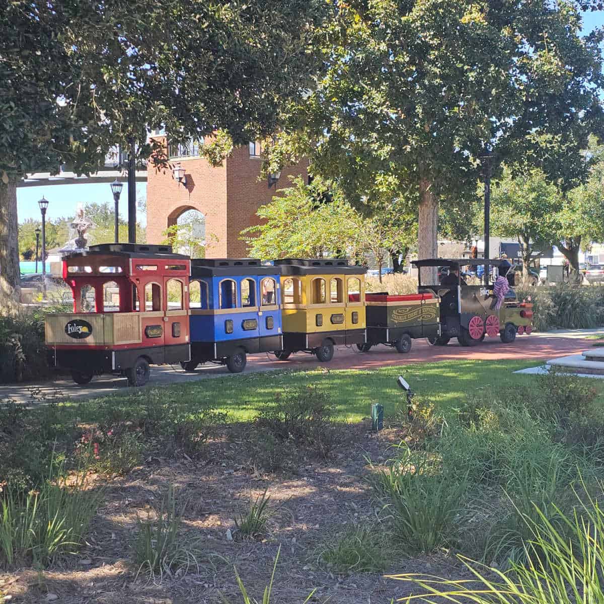 miniature train going through the park with a brick building in the background