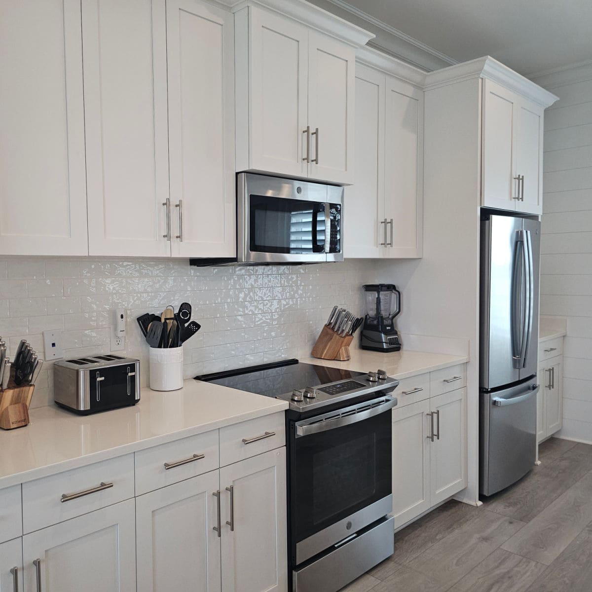 White kitchen cabinets with stainless steel appliances, toaster, blender, and knife block on the white counter