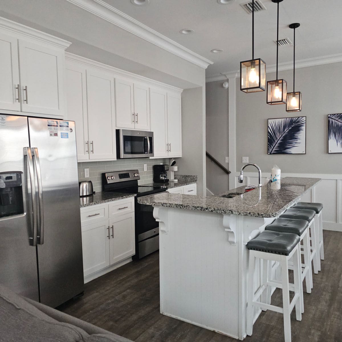 White kitchen cabinets wtih stainless steel appliances, bar stools tucked under the granite counters, lamps over the kitchen island