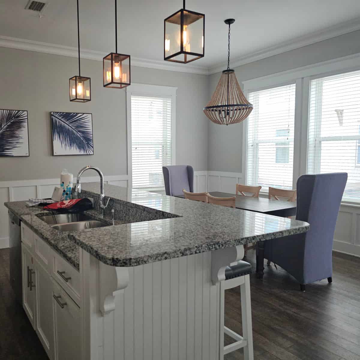 looking over the kitchen island to the dining area with two tall blue chairs and 4 brown chairs around the table