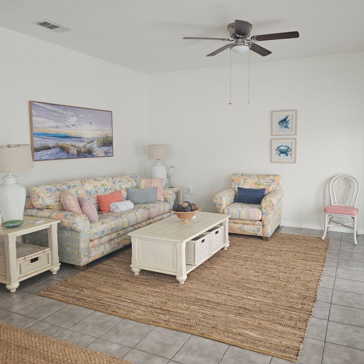 Living room with floral couch, white table in front of the couch, coastal art on the wall