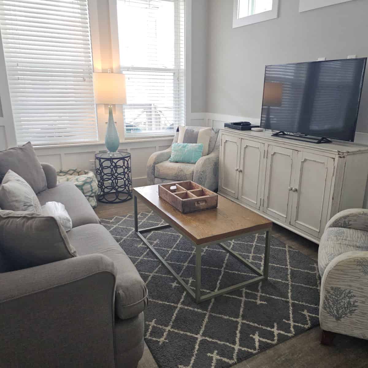 living room with grey couch, table near the couch, white tv console and tv, lamp to the left near the window