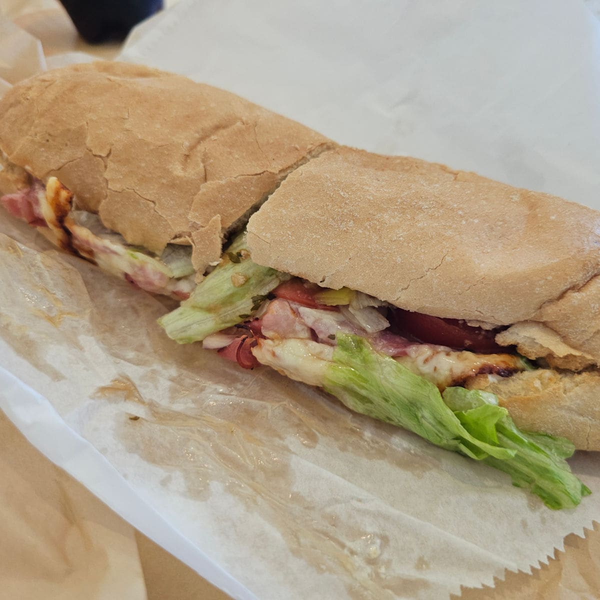 sandwich with meat, cheese, and lettuce on a paper lined table