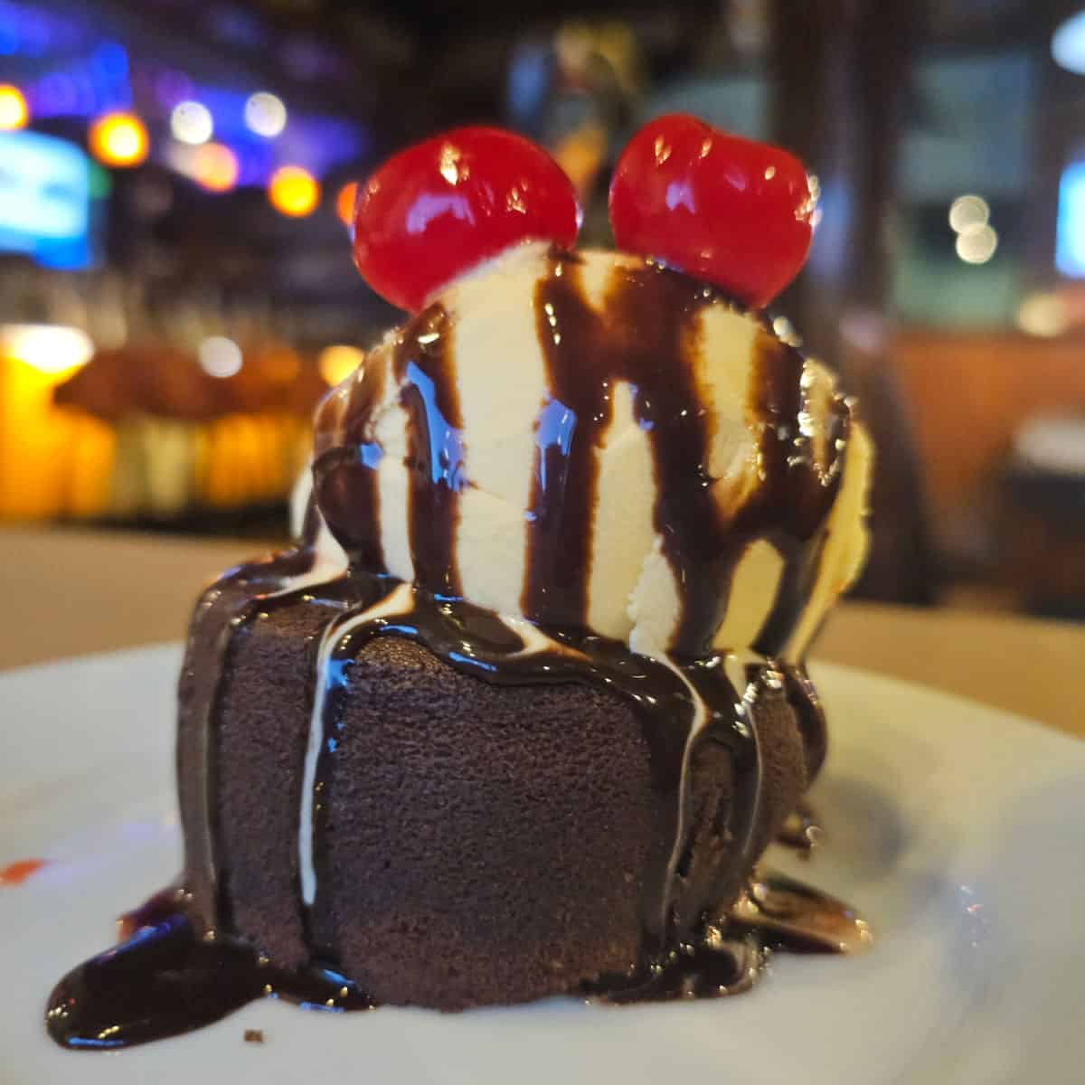 Molten lava cake topped with ice cream, two cherries, and chocolate sauce
