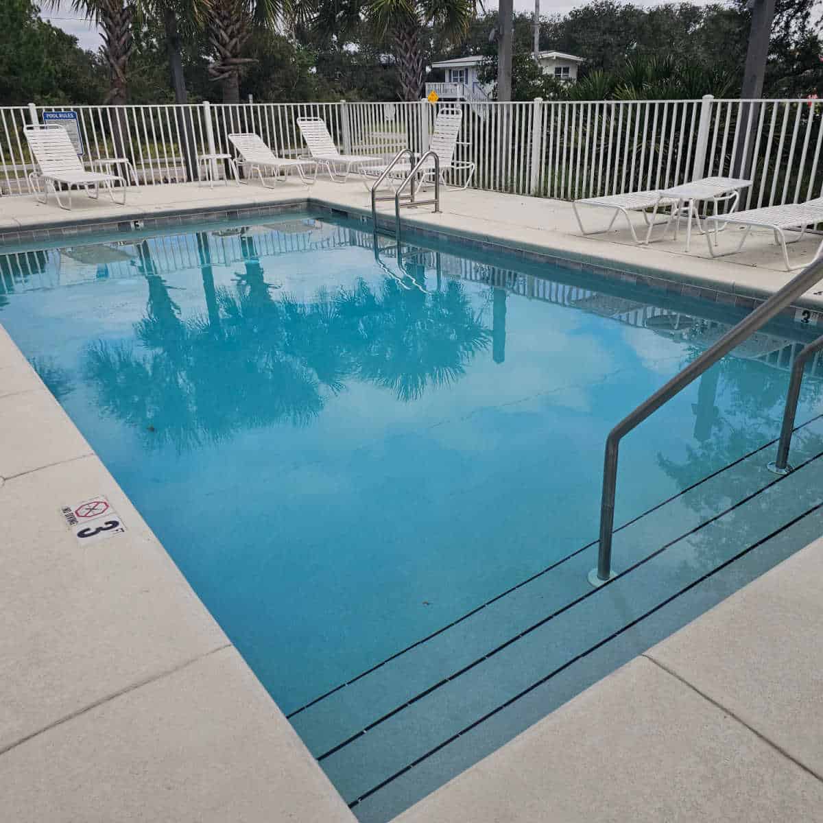 outdoor pool with white deck chairs around the pool deck and a white fence