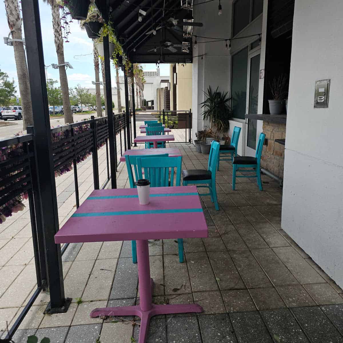 pink tables and blue chairs under a cover with a flower wall towards a parking lot