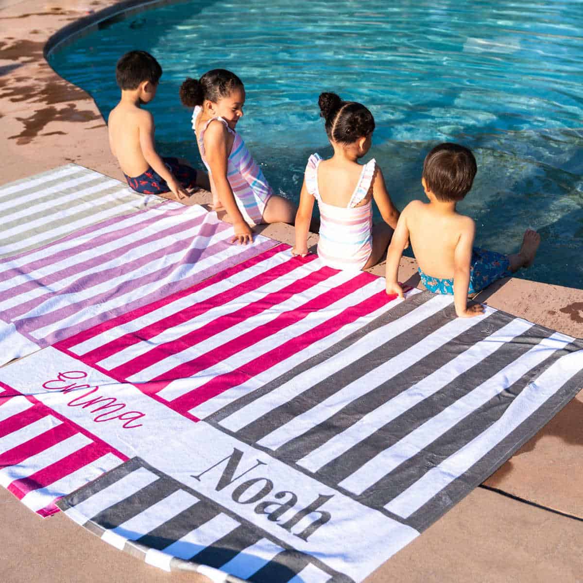 kids sitting on the edge of a pool with personalized towels behind them