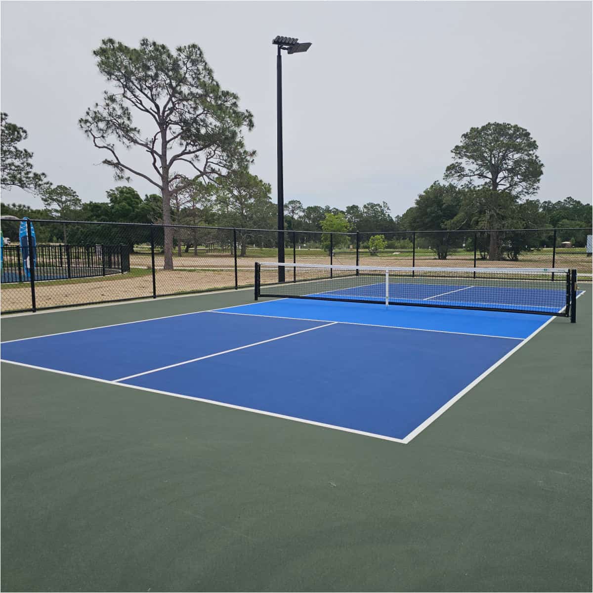 pickledball court behind a dark fence with trees and campsites in the background