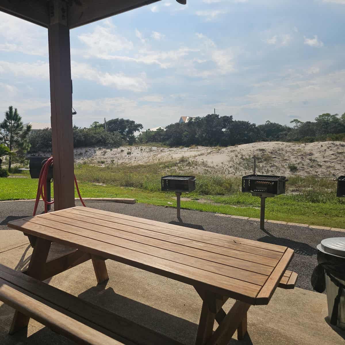looking over a wooden picnic table towards BBQ grills and sand dunes