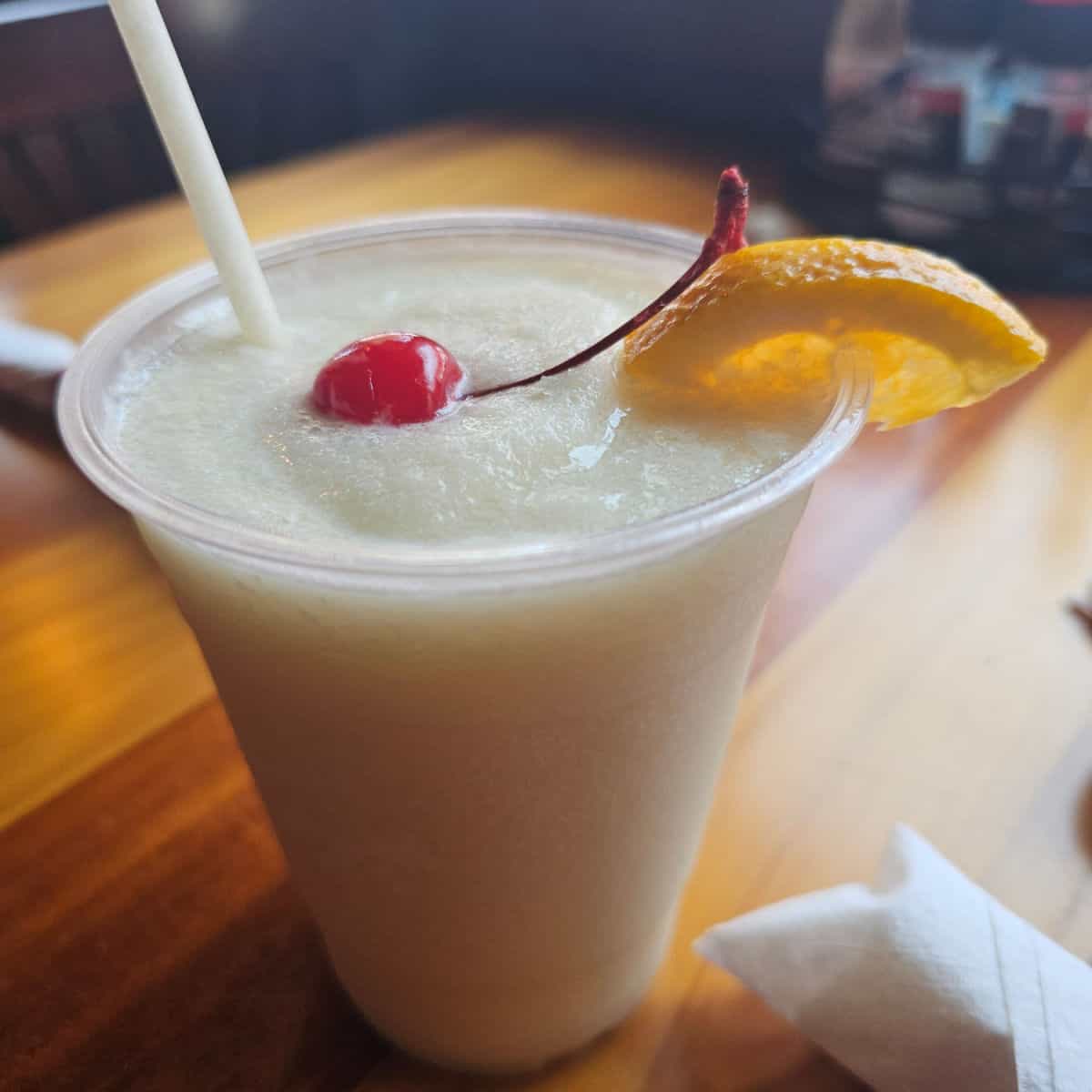 Pina colada in a plastic cup with a cherry and orange slice garnish