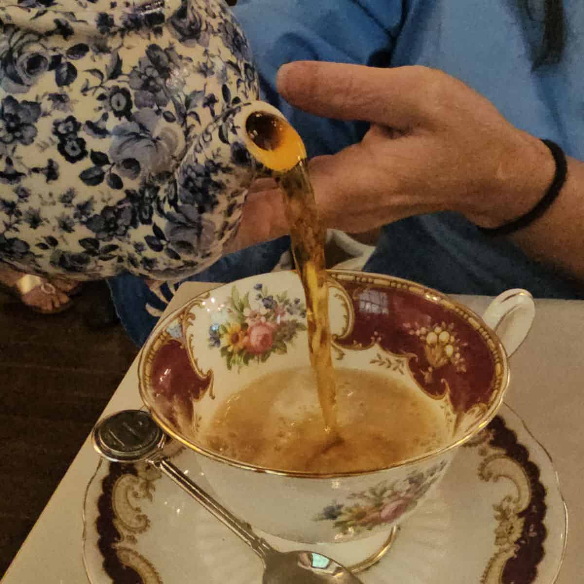 tea pouring from a blue floral teapot into a floral teacup