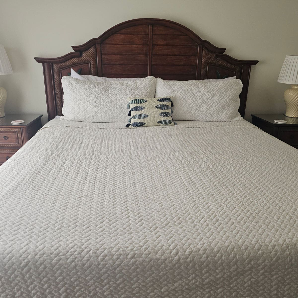 Bedroom with wooden headboard, white linens and pillows, nightstand on either side and white lamps