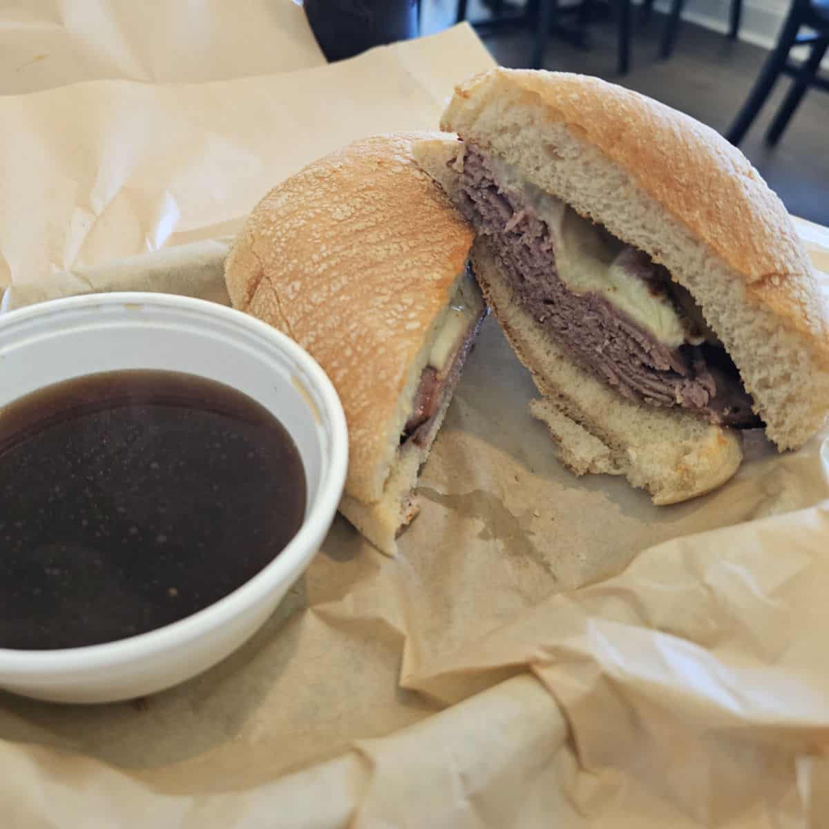 Prime Rib sandwich with a bowl of au jus sauce next to it in a paper lined basket