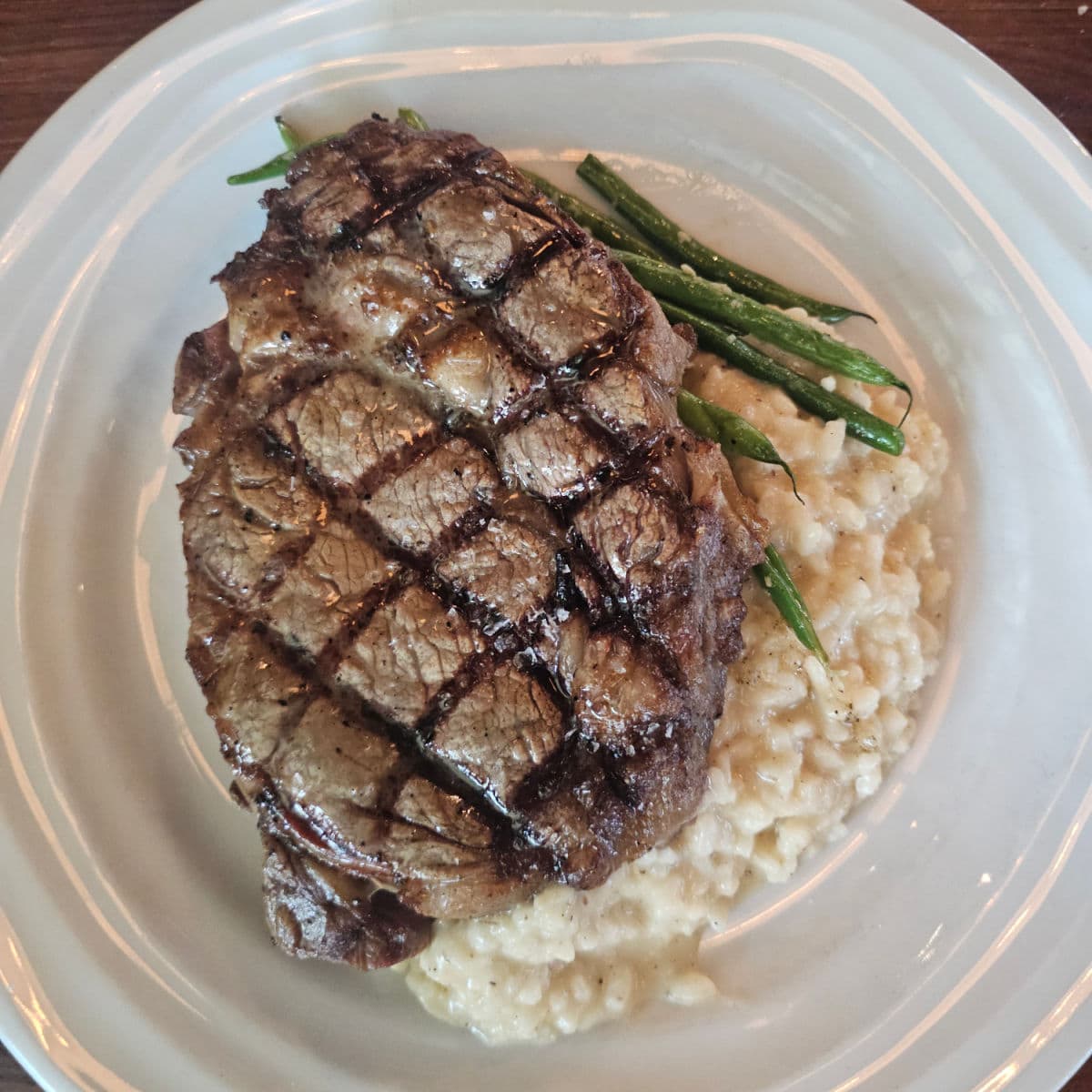 ribeye steak perfectly cooked with parmesan risotto and green beans on a white plate