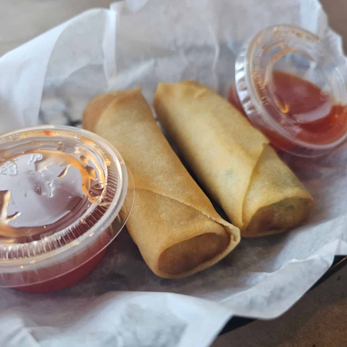 two vegetable spring rolls in a basket with two containers of sauce