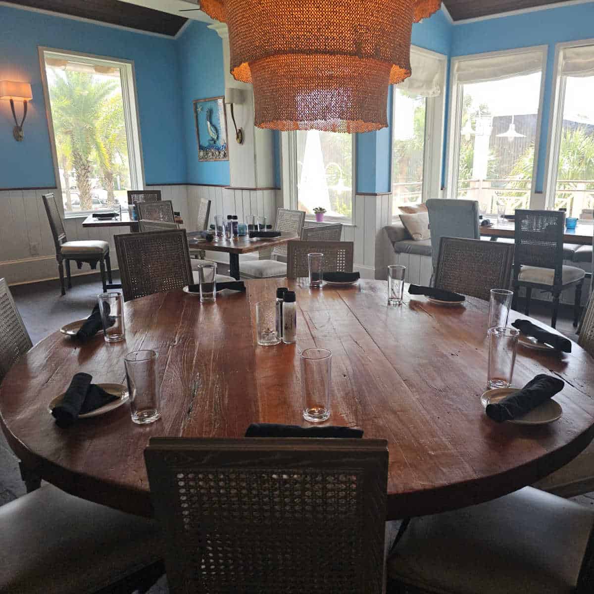 large round table with chandelier above it and other tables, blue walls with coastal art
