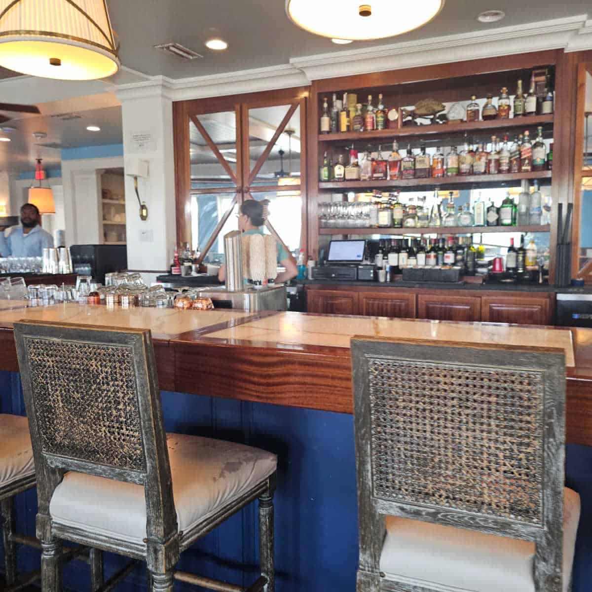 bar seating with tall chairs, bartenders behind the counter, shelves with bottles and glasses
