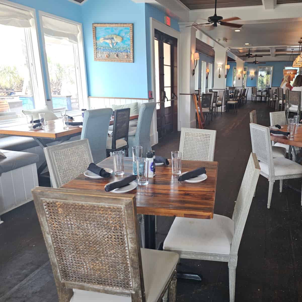 indoor seating with tables and chairs, coastal art of the wall, people sitting at the bar in the top corner