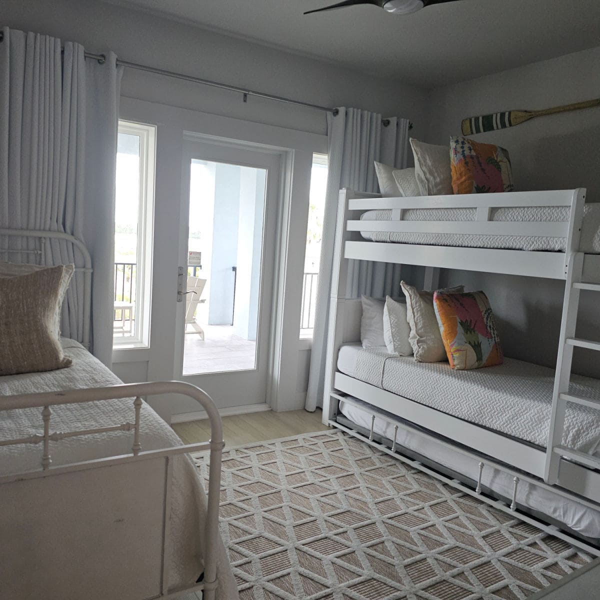 bedroom with a large white bunkbed on one side and a bed on the other, glass door to the balcony