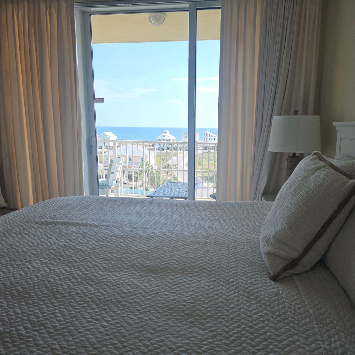 Looking over a bed with white linens to the balcony and views of the Gulf