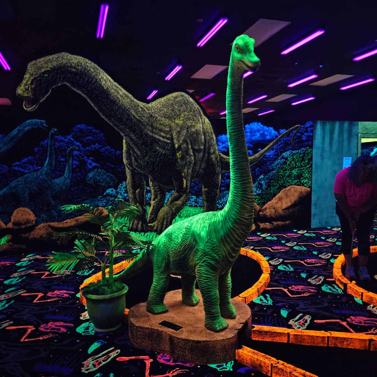 Tall neon dinosaur sculptures and art in a neon blacklight indoor mini golf course