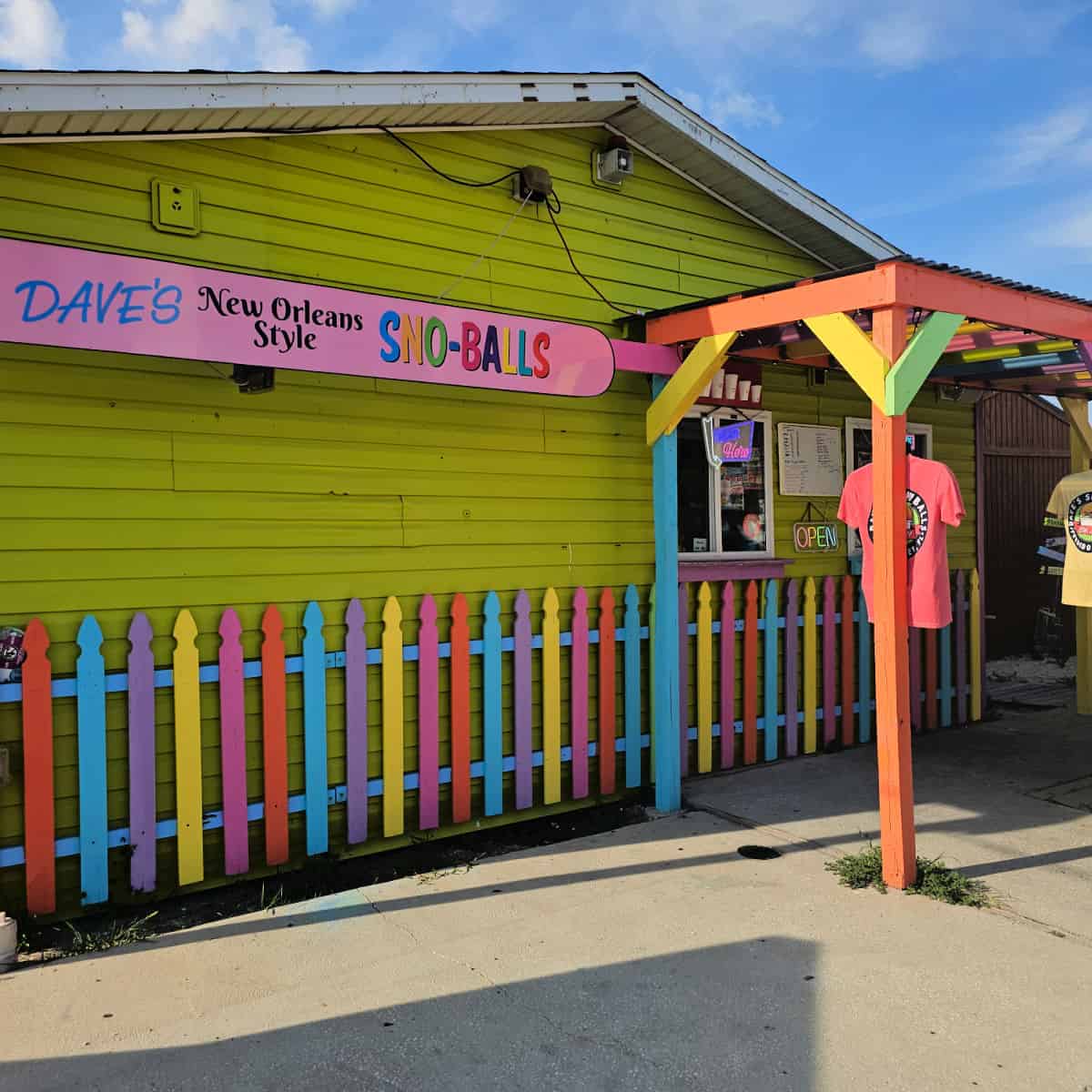 Dave's New Orleans Style Sno-Balls sign on the side of a green building with colorful fence