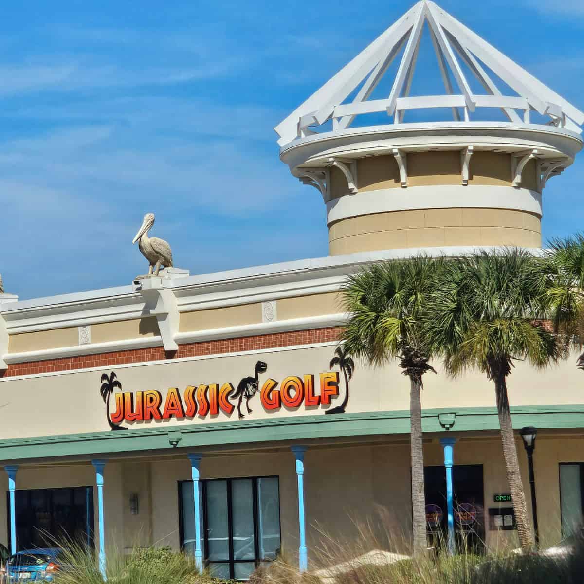 Jurassic Golf sign on the side of a white building with a pelican statue on the roof