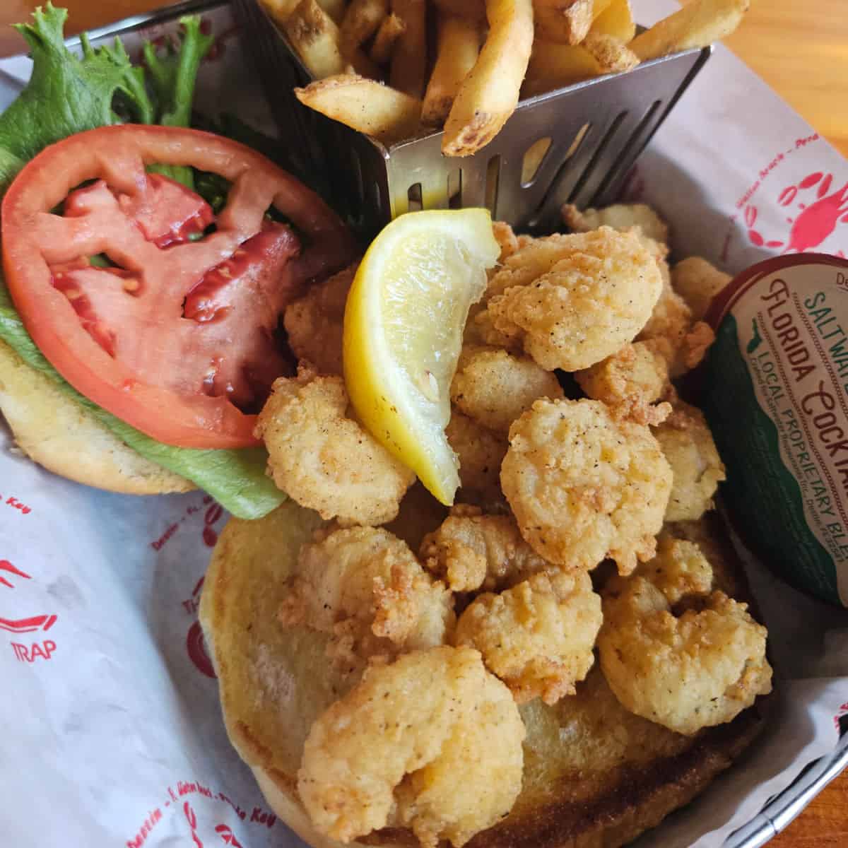 Fried shrimp sandwich with lettuce and tomato next to a cup of fries