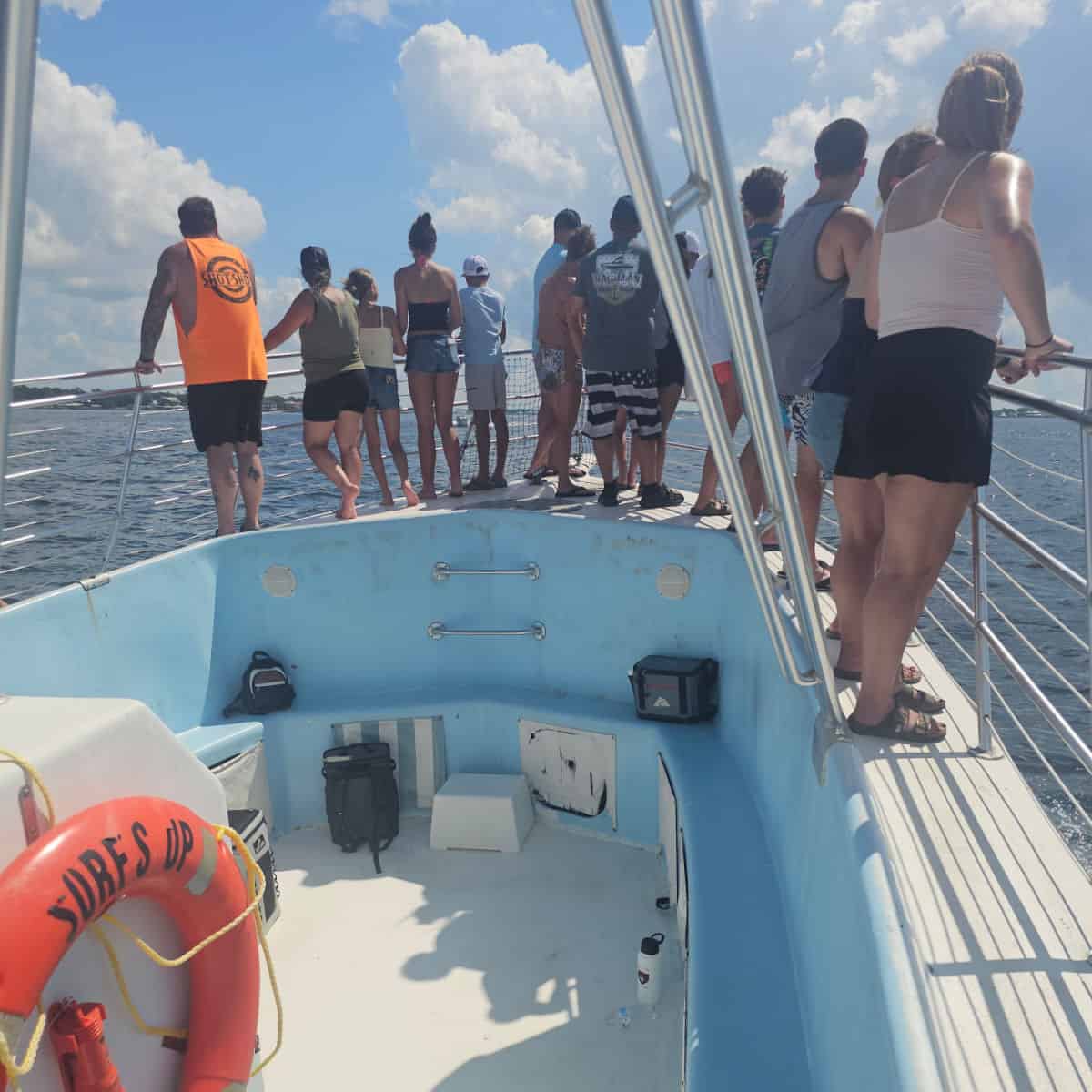 People standing at the front of a blue boat with a Surf's Up life ring