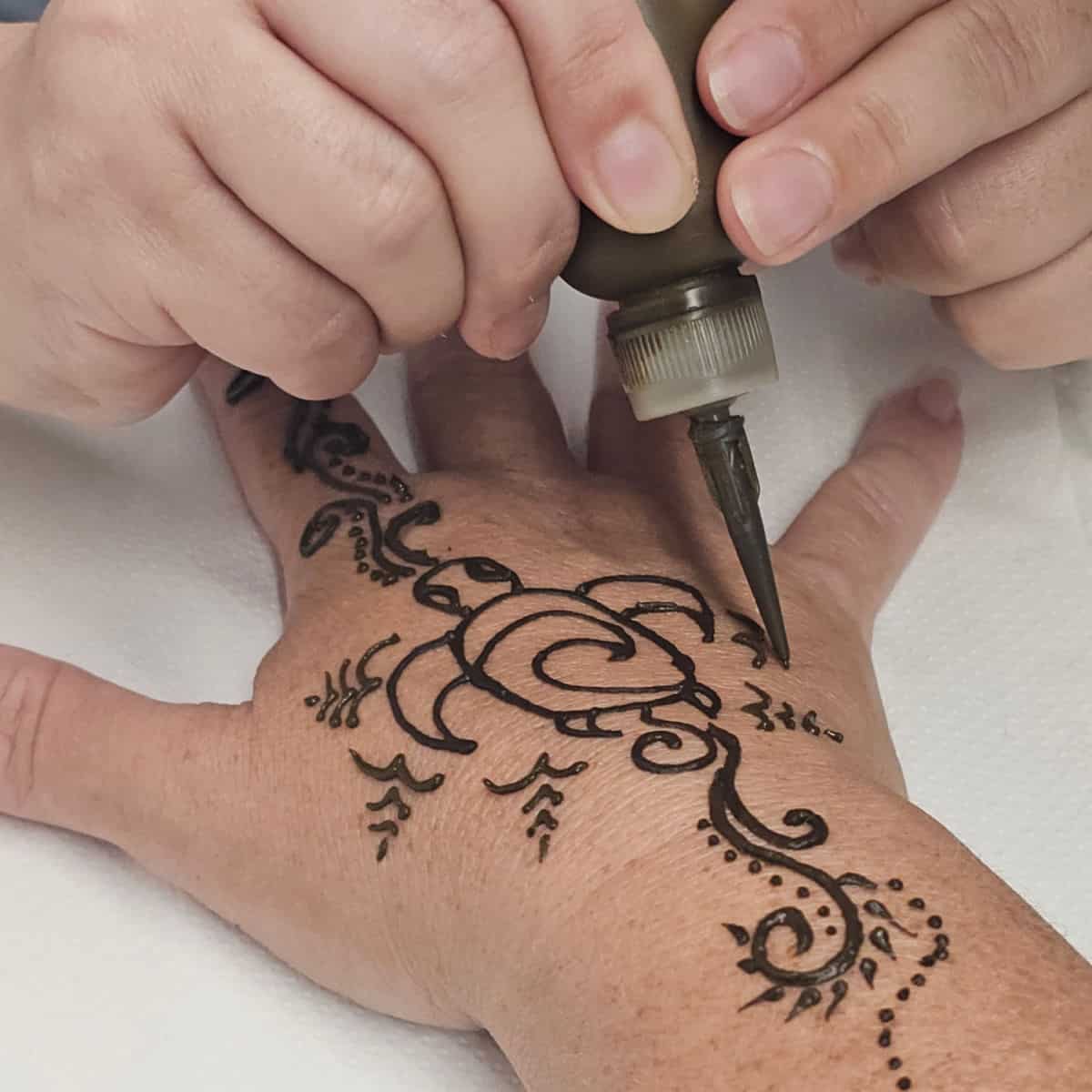 Henna turtle design being painted on a hand