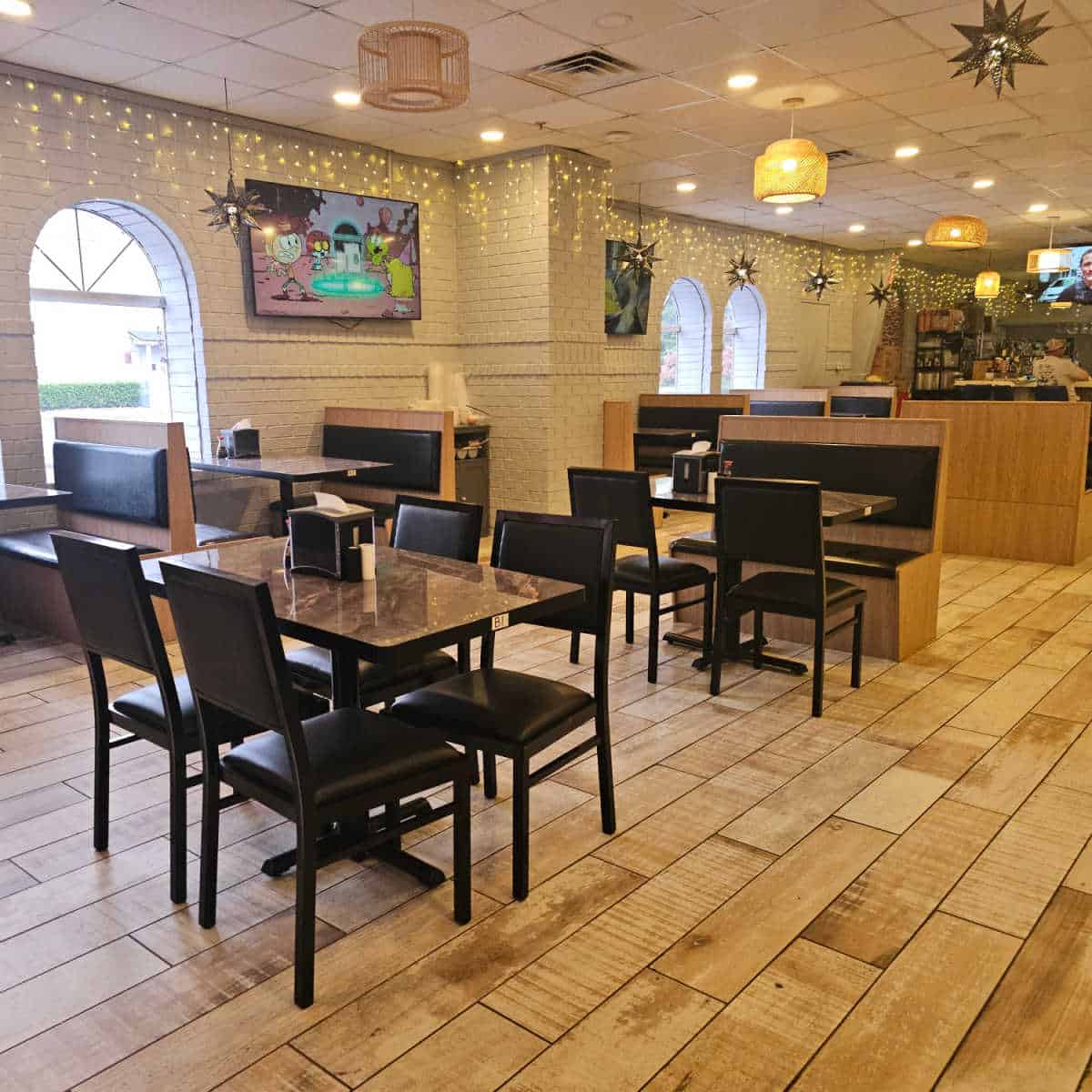 indoor seating with tables and chiars and booths in the restaurant with flatscreen tvs on the wall and a bar in the background