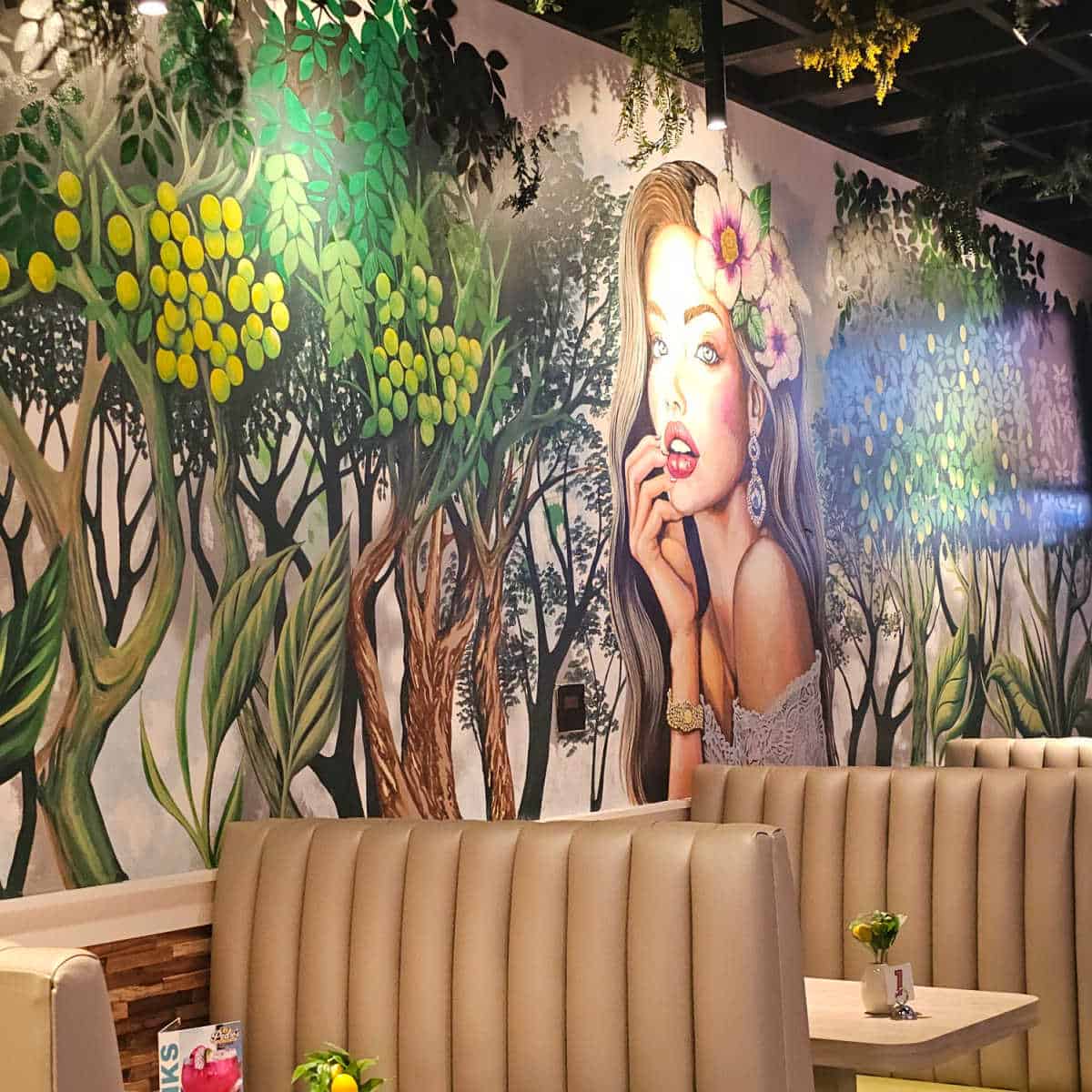 mural with a woman with flowers in her hair, trees along the wall. booths with leather seats under the mural