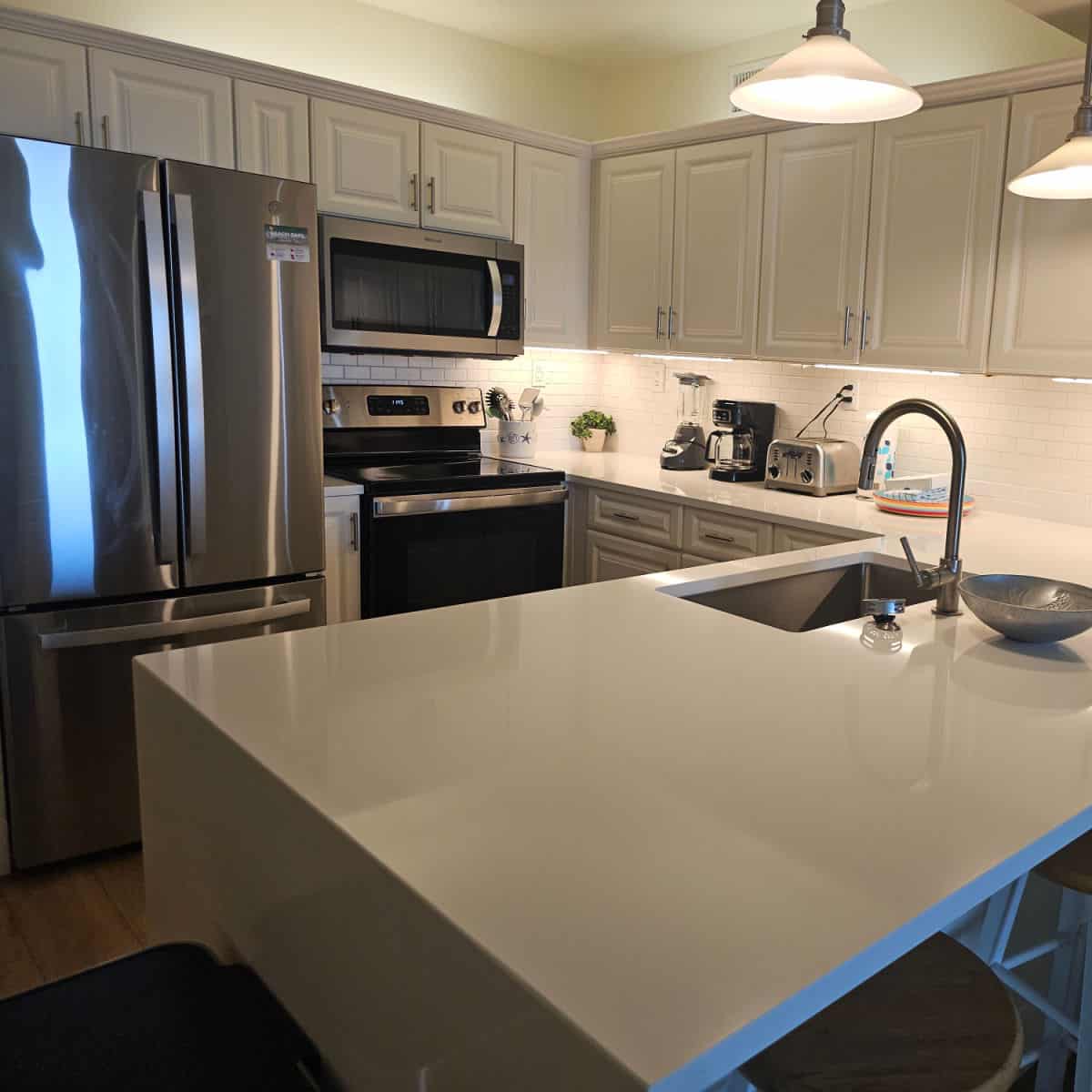 kitchen with white cabinets and counters, stainless steel appliances and a toaster, blender, and coffee maker on the counter